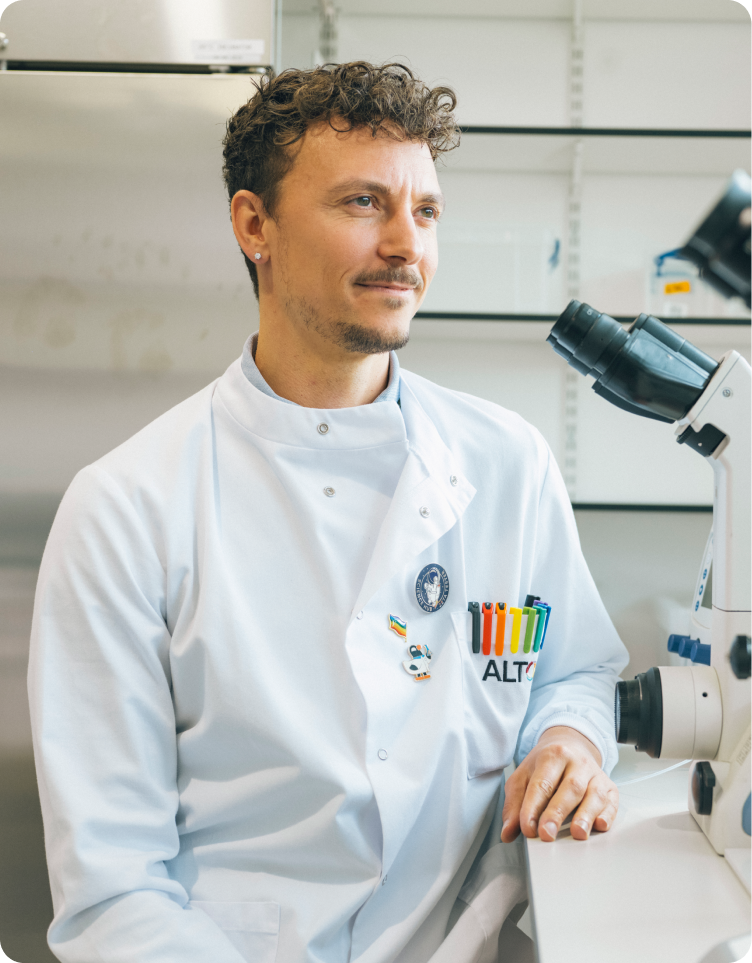 Felix Mayr seated wearing a lab coat in front of a microscope